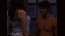 a shirtless man is kissing a woman in front of a window .