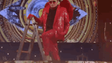 a man in a red suit is standing next to a ladder in front of an eye .