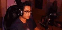 a man wearing headphones and a necklace is sitting in front of a microphone in a room .