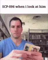 a man in a blue shirt is holding a stack of cards in front of a bookshelf .