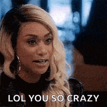 a woman with blonde hair and hoop earrings is sitting at a table and says lol you so crazy .