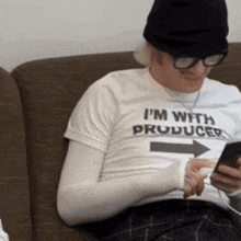 a man wearing a t-shirt that says " i 'm with producer " sits on a couch