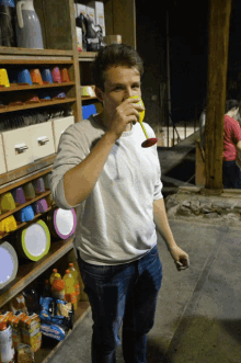 a man drinking from a glass in front of a shelf of cups