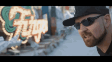 a man wearing sunglasses and a hat stands in front of a neon sign that says ' king '