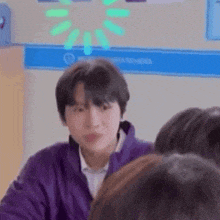 a young man in a purple jacket is sitting in a classroom with a group of people .