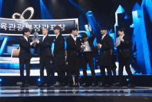 a group of men standing on a stage with a sign in the background that says ' korean '