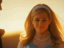 a woman wearing a headband and a pearl necklace is smiling at the camera .