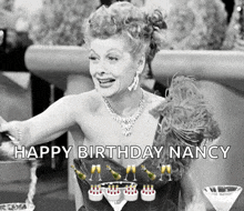a black and white photo of a woman sitting at a table with champagne glasses and a birthday cake .