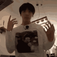 a man wearing a white shirt with a picture of a man on it is standing in a room with his hands outstretched .