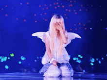 a woman in a white dress with angel wings is kneeling down on a stage