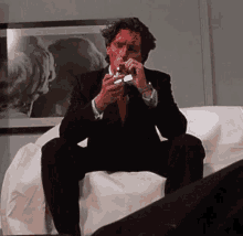 a man in a suit is smoking a cigarette while sitting on a couch .