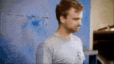 a man in a grey shirt is standing in front of a blue wall with barbed wire on it .