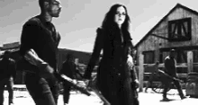 a black and white photo of a man and a woman holding hands in front of a building .