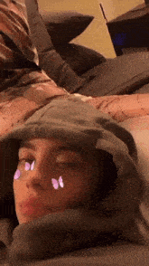 a woman is laying on a bed with butterflies on her face and a hoodie on her head .