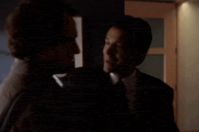 two men are kissing in a dark room in front of a framed painting .