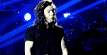 a man with long hair is singing into a microphone on a stage in a dark room .