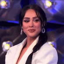 a woman wearing a white jacket and earrings is smiling .
