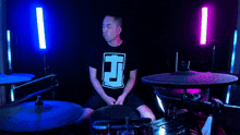 a man wearing a black shirt with the letter t on it is playing drums
