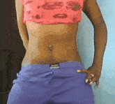 a woman wearing purple shorts and a pink crop top has a piercing in her belly
