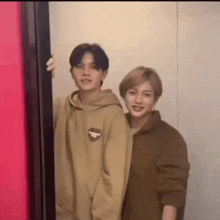 two men are standing next to each other in front of a red wall .