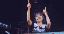 a girl wearing a shirt that says ' aisha ' on it holds her arms in the air