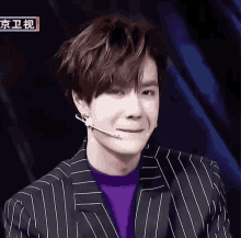 a man wearing a striped suit and a purple sweater with a microphone on his head
