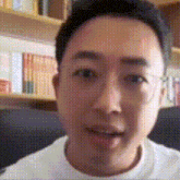 a man is sitting on a couch in front of a bookshelf and smiling .