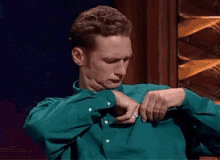 a man in a green shirt is adjusting his shirt collar