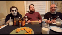 three men are sitting at a table with a plate of chicken nuggets