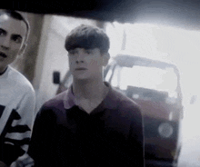 two young men are standing next to each other in front of a car in a garage .