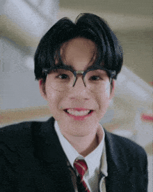 a young man wearing glasses and a suit is smiling for the camera .