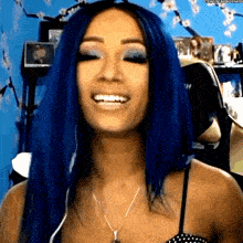 a woman with blue hair is smiling and wearing a necklace and headphones .