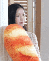 a woman leans against a wall holding a loaf of bread