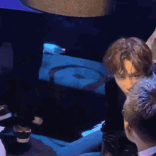 a man in a black jacket is talking to another man in a dark room