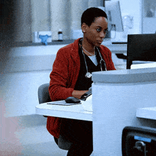 a woman wearing a stethoscope sits at a desk with a computer