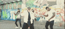 a group of people are dancing in front of a graffiti wall that says ' a '