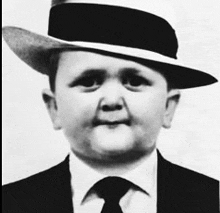a young boy wearing a suit and tie is wearing a hat .