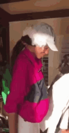 a woman wearing a pink jacket and a hat is standing in a room .