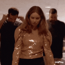 a woman in a sequined top is standing in a hallway with other people .