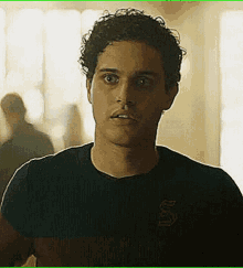 a young man with curly hair is wearing a black and red striped shirt with the letter s on it .