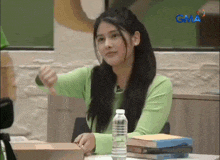 a woman in a green shirt is sitting at a table with books and a water bottle