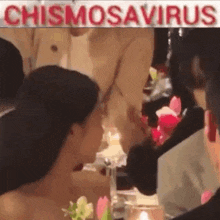 a woman is sitting at a table with flowers and a sign that says chismosaurus .