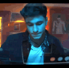 a man in a blue jacket and white shirt is sitting in a dark room looking at something .