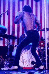 a man with a cross tattoo on his back is singing into a microphone