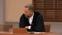 a man in a judge 's robe sits at a table with a microphone in front of him