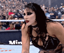 a woman is standing in a wrestling ring with the word min on the wall behind her .
