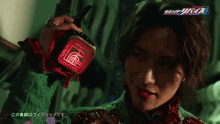 a man in a green shirt holds a red object in his hand with chinese writing on it