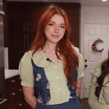 a woman with red hair is wearing a green shirt and blue vest