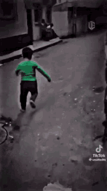 a little boy in a green shirt is running down the street .