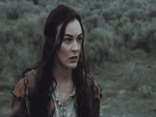 a woman with long dark hair stands in a field